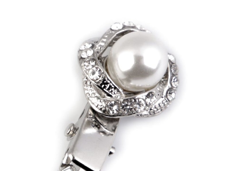 May include: A silver hair clip with a pearl and crystal embellishment. The pearl is white and the crystals are clear.