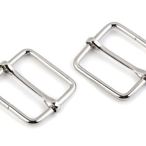 May include: Two silver metal buckle closures for straps or belts. The buckles are rectangular with a smooth finish.