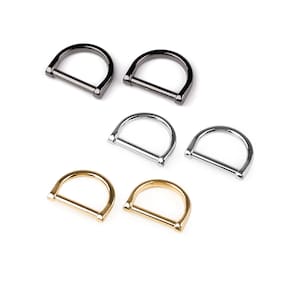 Può includere: Cinque anelli a D in diverse finiture: nero, argento e oro. Gli anelli sono tutti della stessa dimensione e forma.