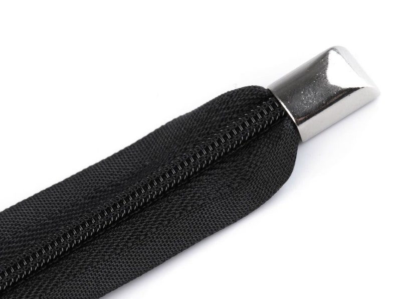 May include: A black zipper with a silver metal pull tab. The zipper is closed and the pull tab is at the top of the zipper.