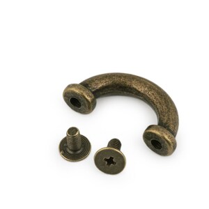 May include: A bronze-colored metal handle with two screws. The handle is shaped like a U and has a rounded edge. The screws are small and have a Phillips head.