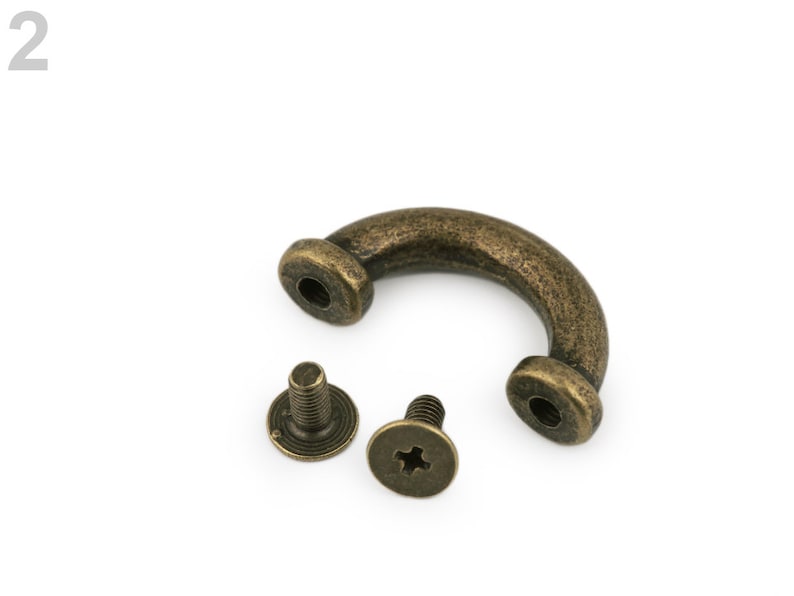 May include: A bronze-colored metal handle with two screws. The handle is shaped like a U and has a rounded edge. The screws are small and have a Phillips head.