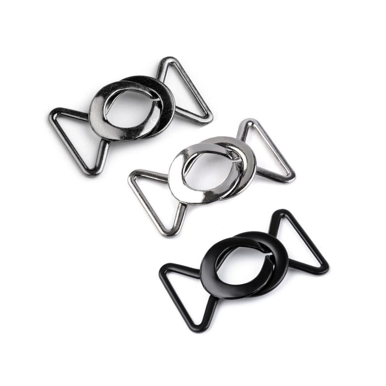 May include: Three metal clasps, two silver and one black, with a circular design. The clasps are designed for attaching straps or fabric.
