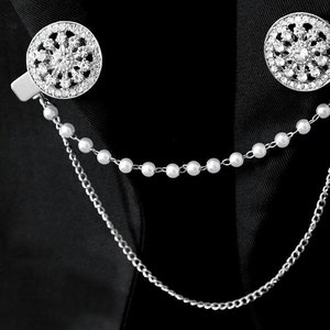 May include: A silver chain with a pearl strand and two round, silver, rhinestone-encrusted brooches.