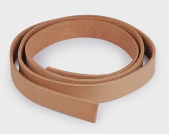 Puede incluir: Una tira enrollada de cuero de color tostado claro con un acabado liso y mate en la superficie exterior y un grano natural texturizado en el lado interior. La correa de cuero es uniforme en ancho y grosor, formando una figura circular.