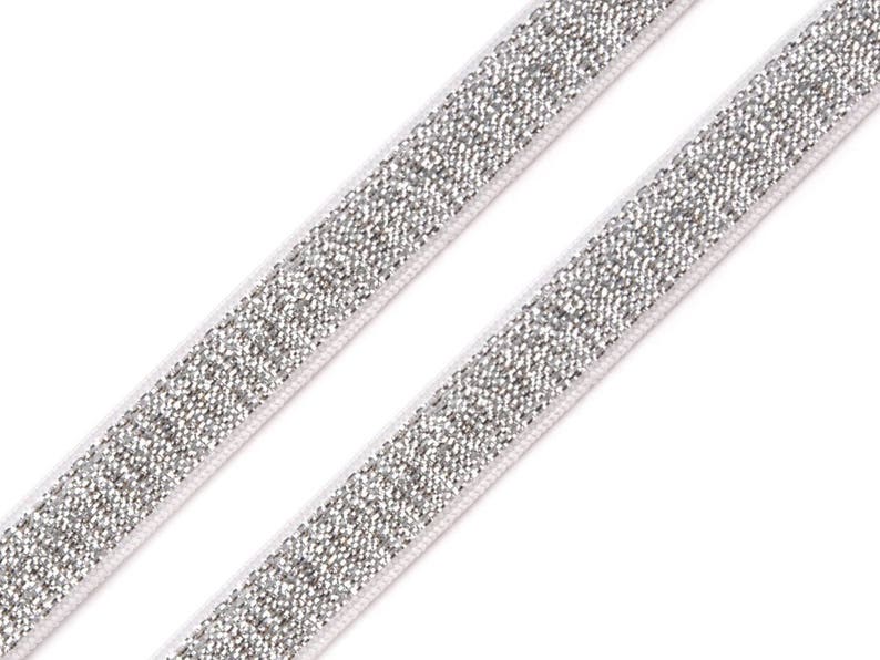 May include: Two silver glitter elastic bands on a white background. The bands are angled diagonally across the frame. The glitter is densely packed, creating a shimmering effect. The edges of the bands are bordered with a thin white line.