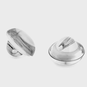 Pode incluir: Dois objetos prateados de forma abstrata. Um é oval com uma base arredondada e um pequeno orifício. O outro tem uma forma arredondada, semelhante a um pires, com um design central pontiagudo. Ambos têm uma aparência reflexiva e marmoreada.