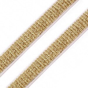 May include: Two strips of gold glitter elastic ribbon on a white background. The ribbon is made of small, sparkling gold particles and is bordered by a thin white edge. The ribbon is angled diagonally across the frame.