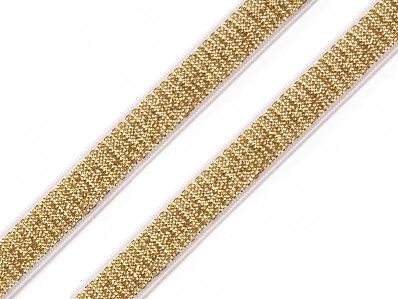 May include: Two strips of gold glitter elastic ribbon on a white background. The ribbon is made of small, sparkling gold particles and is bordered by a thin white edge. The ribbon is angled diagonally across the frame.