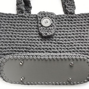 May include: Gray crocheted tote bag with a gray leather bottom and a gray button closure.