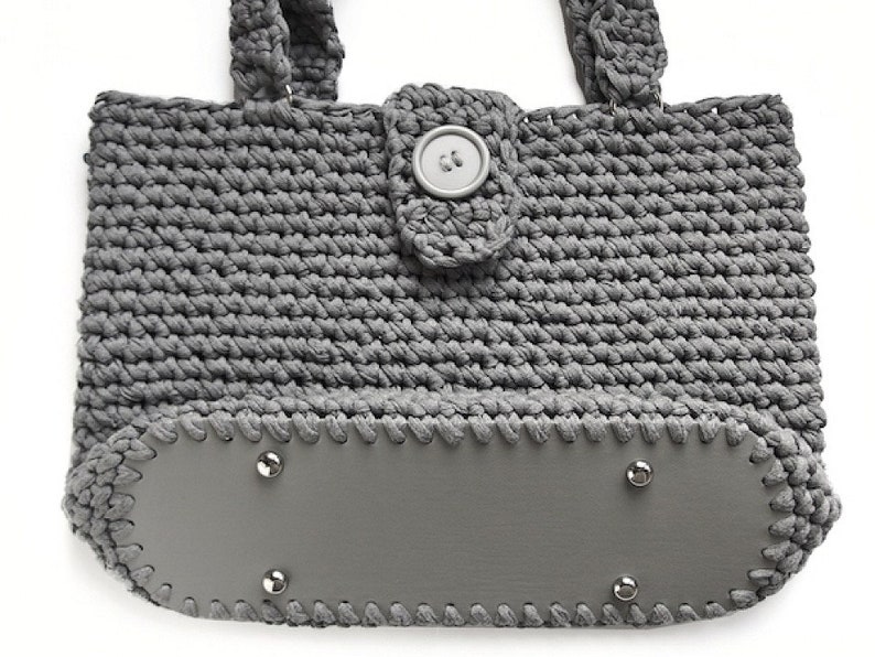 May include: Gray crocheted tote bag with a gray leather bottom and a gray button closure.