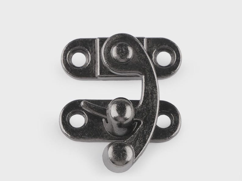 May include: A dark gray metal clasp with a curved latch and two mounting plates, each with two holes for screws. The clasp is designed to secure a box or container.