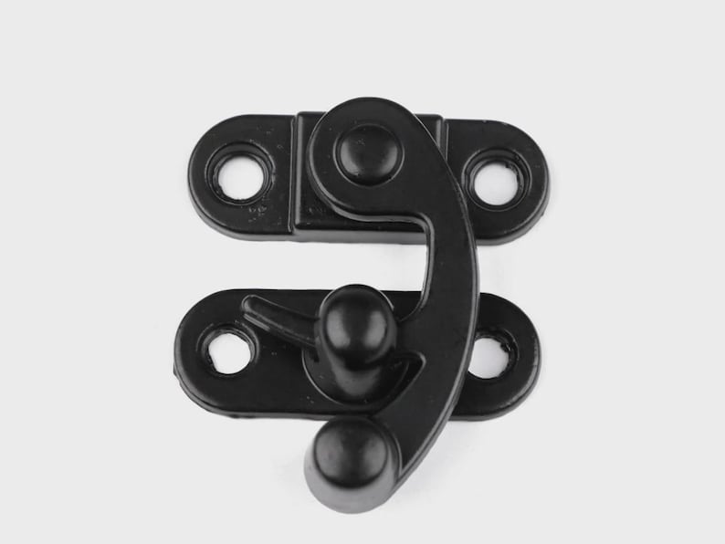 May include: A black metal clasp with a curved latch and two mounting plates, each with two holes for screws. The clasp is designed to secure a box or container.