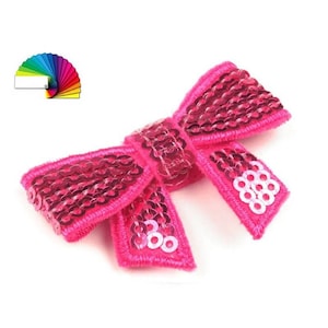 Peut inclure: Un nœud rose pailleté avec une finition brillante. Le nœud est fait de tissu et a une boucle à l'arrière pour l'attacher à un vêtement ou à un autre article.