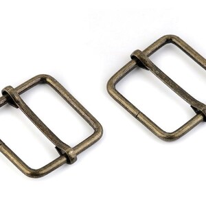 May include: Two antique gold metal belt buckle slides. The slides are rectangular with a smooth finish.