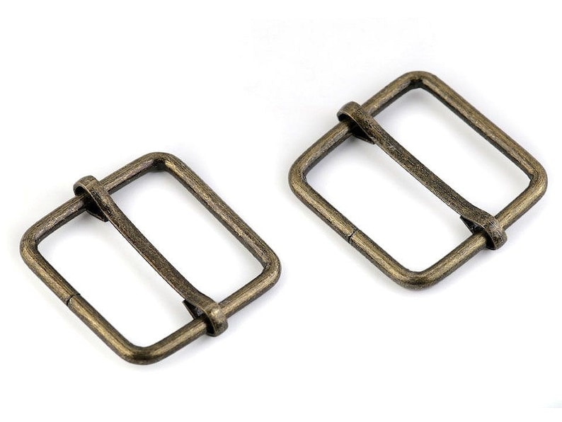 May include: Two antique gold metal belt buckle slides. The slides are rectangular with a smooth finish.