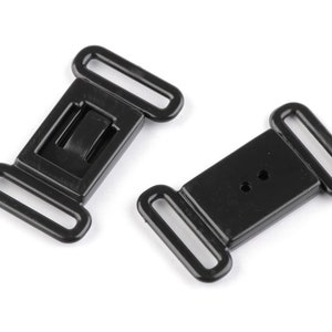 Op de afbeelding: Twee zwarte plastic gespen met twee lussen aan elke kant. De gespen zijn rechthoekig van vorm met een kleine rechthoekige opening in het midden.