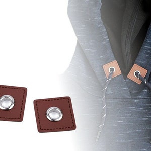 Può includere: Due quadrati in pelle marrone con occhielli argentati e cuciture. I quadrati sono utilizzati per fissare i lacci di serraggio ai vestiti.