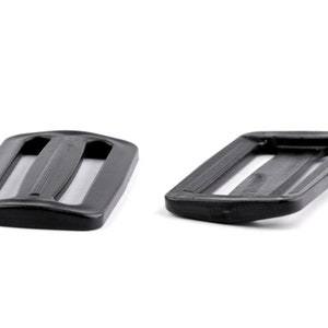 Peut inclure: Deux boucles coulissantes en plastique noir. Les boucles sont rectangulaires avec des bords arrondis et ont trois fentes pour une sangle.