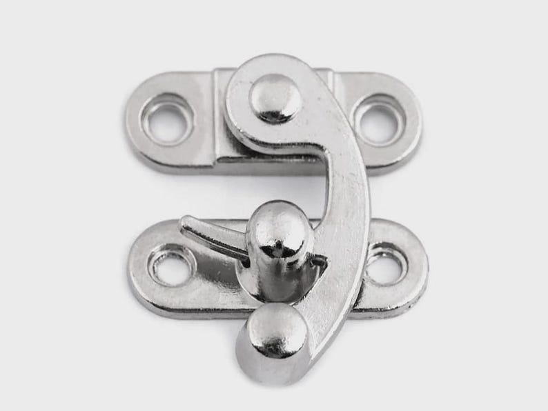 May include: A shiny, silver-colored metal clasp with a curved hook and two mounting plates, each with two holes for screws. The clasp is designed to secure a box or container.