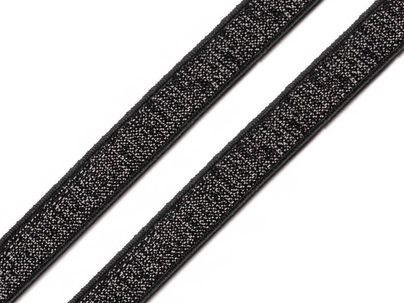 May include: Two black elastic bands with a sparkly silver texture. The bands are angled diagonally across a white background. The bands are likely used for sewing or crafting projects.