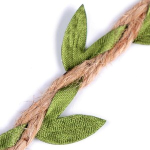 May include: A close-up of a brown jute twine garland with green fabric leaves. The leaves are sewn onto the twine and are arranged in a repeating pattern.