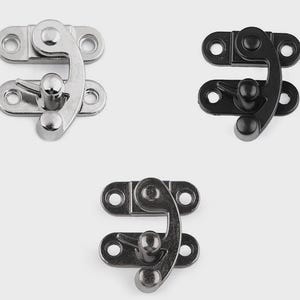 May include: Three metal clasps in silver, black, and gunmetal gray. Each clasp has a curved hook and a rounded knob for securing. The clasps are designed with two plates, each with three holes for mounting.