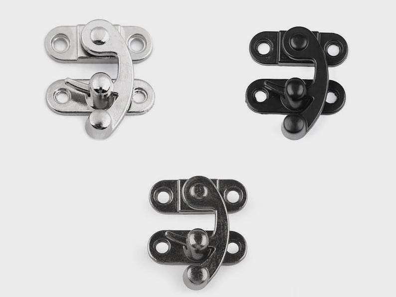 May include: Three metal clasps in silver, black, and gunmetal gray. Each clasp has a curved hook and a rounded knob for securing. The clasps are designed with two plates, each with three holes for mounting.