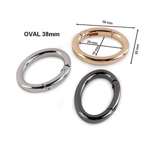 May include: Three oval-shaped metal clasps, one silver, one gold, and one black. The gold clasp is 38 mm in diameter and has measurements of 29 mm and 19 mm marked on it.