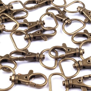 May include: A group of antique gold-toned metal key rings with a swivel clasp and a D-ring. The key rings are scattered on a white surface.