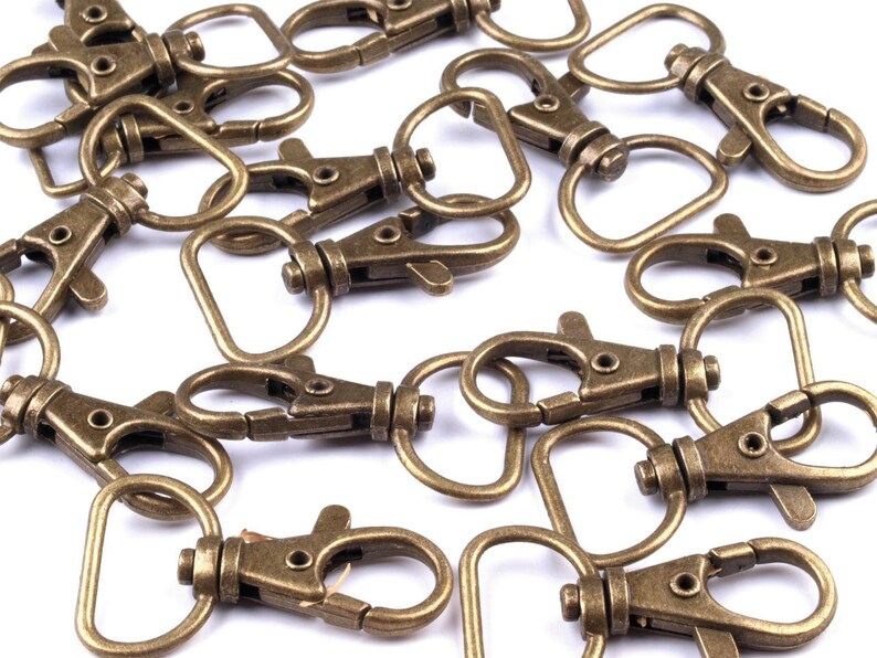 May include: A group of antique gold-toned metal key rings with a swivel clasp and a D-ring. The key rings are scattered on a white surface.