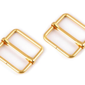 May include: Two gold-colored metal buckle closures. The buckles are rectangular with a smooth finish.