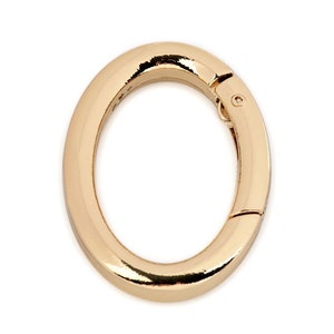 May include: Gold-toned metal oval ring with a spring-loaded clasp. The ring is smooth and shiny.