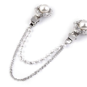 May include: A silver chain with two pearl and rhinestone accents. The chain has two clasps, one on each end.