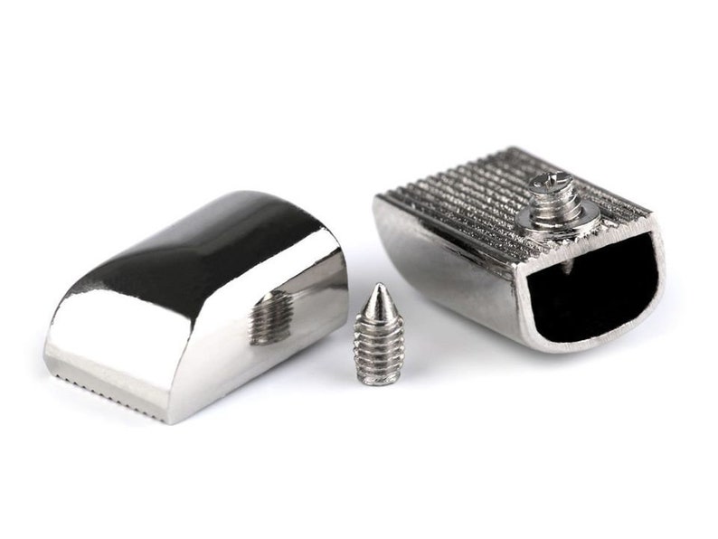 May include: Three silver metal pieces, including a small screw, a curved piece with a textured edge, and a rectangular piece with a textured top and a hollowed-out section.