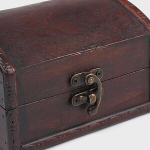 May include: A small, dark brown wooden chest with a curved top and decorative trim. The chest features a metal clasp and hinges, suggesting a vintage or antique style. The wood grain is visible, adding to its rustic charm.