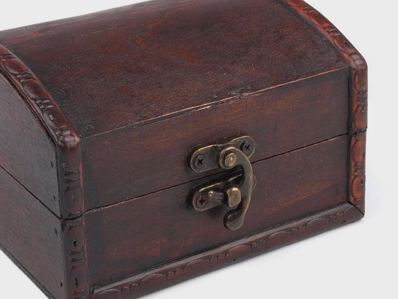 May include: A small, dark brown wooden chest with a curved top and decorative trim. The chest features a metal clasp and hinges, suggesting a vintage or antique style. The wood grain is visible, adding to its rustic charm.