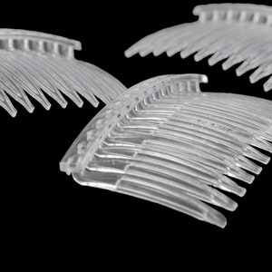Könnte beinhalten: Drei durchsichtige Plastikhaarkämme mit einer gebogenen Form und feinen Zähnen. Die Kämme sind übereinander gestapelt, wobei der obere Kamm die darunter liegenden Kämme teilweise verdeckt.