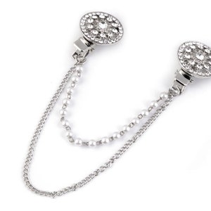 May include: A silver chain with two round, rhinestone-encrusted clasps. The chain is made of two strands, one with small pearls and one with a more traditional chain link.