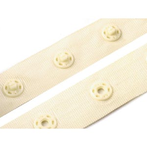 Puede incluir: Primer plano de dos tiras de tela blanquecina con broches de presi&oacute;n color crema espaciados uniformemente. Los broches tienen un dise&ntilde;o circular con un tornillo central. La tela tiene una textura tejida.