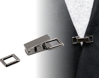 May include: A silver-toned metal clasp with a spring-loaded mechanism. The clasp is designed to be used for attaching two pieces of fabric together. The clasp is shown closed on a piece of black fabric.