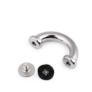Könnte beinhalten: Ein silberner D-Ring aus Metall mit zwei Schrauben. Der D-Ring hat einen Durchmesser von etwa 2,5 cm. Die Schrauben sind etwa 1,25 cm lang.