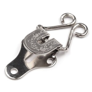 May include: Silver metal hook and eye closure with a floral design. The hook has two loops and the eye has a decorative floral pattern.