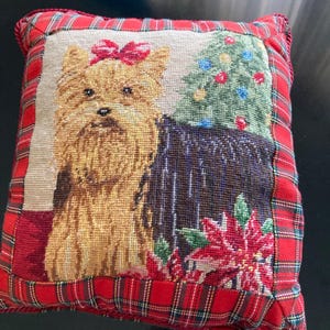 Puede incluir: Cojín decorativo cuadrado con un diseño de tapiz que presenta un Yorkshire Terrier con un lazo rojo, un árbol de Navidad y flores de Pascua. El cojín tiene un borde a cuadros rojo con un ribete de cuerda roja.