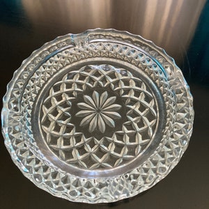 Puede incluir: Un cenicero de vidrio transparente con un patrón de diamante y un diseño de flor en el centro.