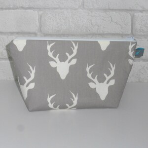 May include: A gray zippered pouch with a white deer silhouette pattern. The pouch has a blue zipper pull.