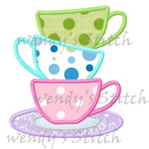 May include: A stack of three teacups with a saucer. The top cup is green with white polka dots, the middle cup is blue with white polka dots, and the bottom cup is pink with white polka dots. The saucer is purple with a floral pattern.