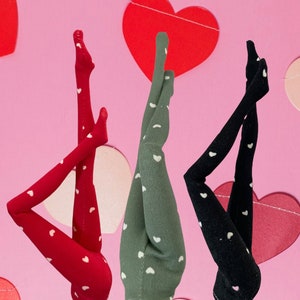 May include: Three pairs of tights with white heart patterns. One pair is red, one is green, and one is black.