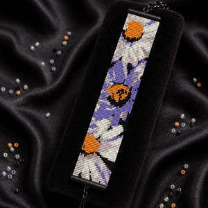 Op de afbeelding: Een rechthoekige kralenarmband met een bloemenpatroon van witte, paarse en oranje kralen. De tekst "Bracelet Bead Pattern", "PDF - Instant Download", "LOOM STITCH" en "Miyuki Delica 11/0 - Color Chart - Word Chart" is zichtbaar.