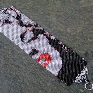Puede incluir: Un brazalete de cuentas con una imagen en blanco y negro de la cara de una mujer con labios rojos. El brazalete tiene un cierre plateado.